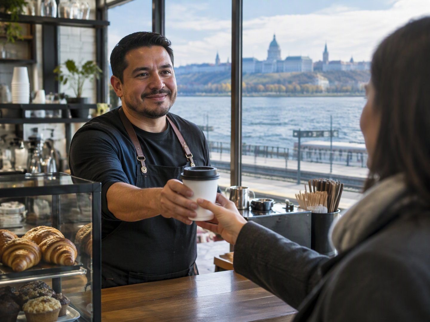 A Rensselaer coffee shop owner handing a coffee to a commuter with the Hudson River behind